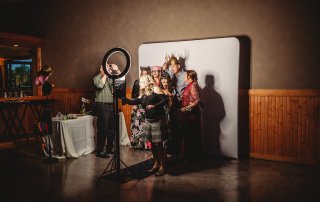 A group of people in costumes poses for a photo in front of a backdrop, while a person adjusts a ring light nearby.